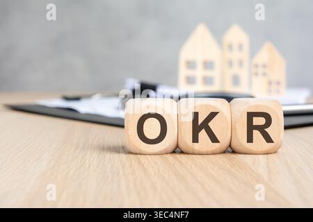 OKR Objectives and Key Results text on wooden blocks, blurred houses and documents. Real estate business strategy and planning concept. Stock Photo