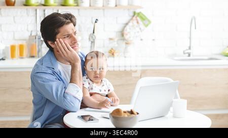 Man Working From Home With Baby in Cozy Kitchen Setting During Daytime Hours Stock Photo