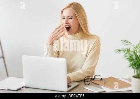 Woman Yawning While Working on Laptop in Modern Office Space During Daytime Stock Photo