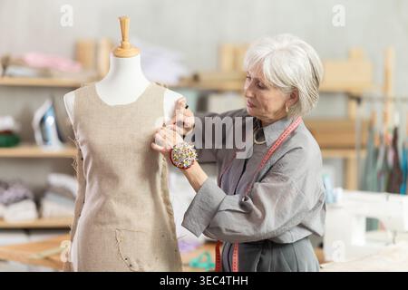 Mature female dressmaker working with mannequin in sewing workshop Stock Photo