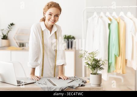 Fashion Designer Working in Studio With Sewing Tools and Clothing on Display Stock Photo