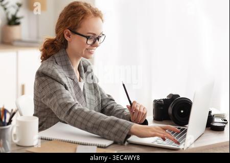 Young Woman Working on Laptop While Taking Notes in Stylish Workspace With Camera Stock Photo
