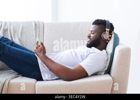 Relaxed Young Man Enjoying Music While Lounging on Couch During Daytime Stock Photo