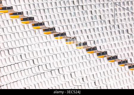 Rows of white stadium seats create a geometric pattern, interrupted by a diagonal line of seats. Repetitive seating arrangement forms a striking visua Stock Photo