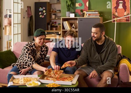 Young adult students sharing pizza while studying together in apartment, representing campus lifestyle and friendship. Useful for education marketing, student housing, youth campaigns Stock Photo
