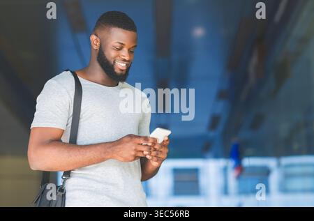 Young Man Smiles While Using Smartphone in Modern Urban Environment Stock Photo