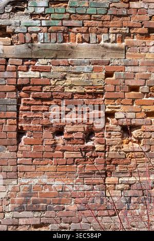 Weathered bricked up window in old brick wall with wooden beam and green patina above, showing aged urban architecture in vertical composition. Stock Photo