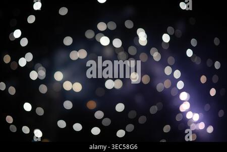 Abstract blurred glowing white and silver bokeh lights from defocused fireworks on dark night sky. Ideal for festive backgrounds celebration overlays Stock Photo