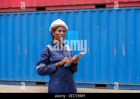 Focused African ethnicity woman supervisor checking inventory data on electronic device for supply chain management at cargo yard, perfect for technol Stock Photo