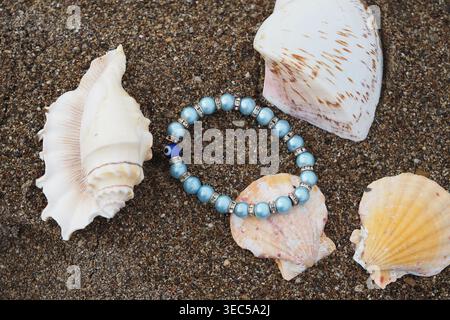 Beads placed among seashells on sandy beach Stock Photo