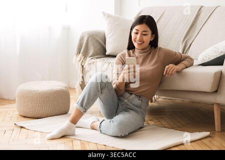 Happy Asian Girl Messaging on Phone at Home Stock Photo