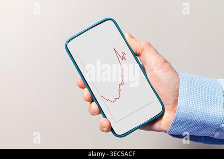 Hand holding a smartphone displaying a red line graph showing market volatility and decline Stock Photo