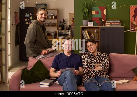 Portrait of diverse college students studying together at home, holding notes and smiling at camera, representing shared learning and youth lifestyle. Ideal for education marketing and campus life Stock Photo