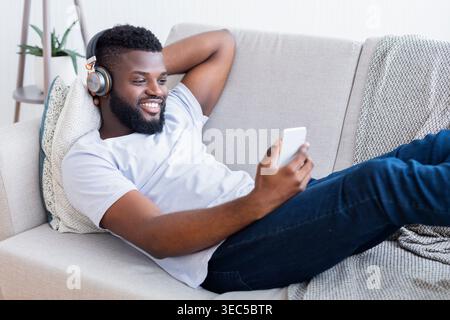 Relaxing Man Listens to Music While Using Smartphone on a Cozy Couch at Home Stock Photo