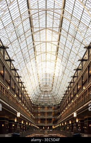 A large atrium in a historic building with a glass ceiling. The warm light from the setting sun illuminates the space, highlighting the architecture. Stock Photo