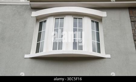 four panel curved white bay window on grey stucco wall, architectural window with upper and lower ledge, low angle view, real estate and modern Stock Photo