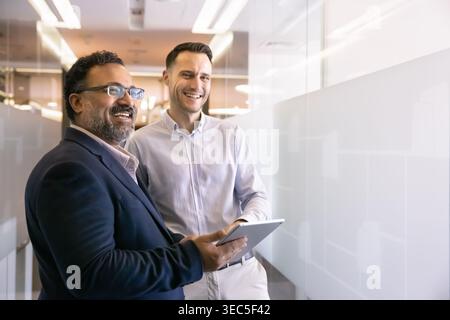 Two happy multiethnic team members standing together in office hallway Stock Photo