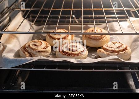 Cinnamon rolls baking in oven on tray with parchment paper, homemade pastry cooking process in warm kitchen light Stock Photo