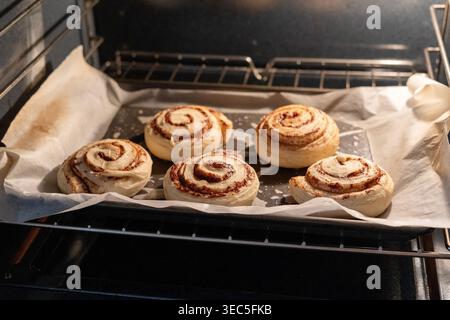 Cinnamon rolls baking in oven on tray with parchment paper, homemade pastry cooking process in warm kitchen light Stock Photo