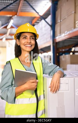Worker wearing hardhat safety vest holding digital tablet in warehouse Stock Photo
