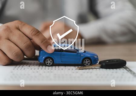 Auto insurance coverage and vehicle protection concept with agent hand presenting blue car model on policy contract document beside car key and shield Stock Photo