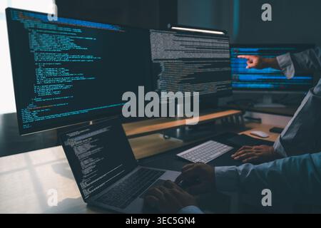 man programmer writing program code at a multi monitor workstation with laptop and software code on screens, performing debugging, software developmen Stock Photo
