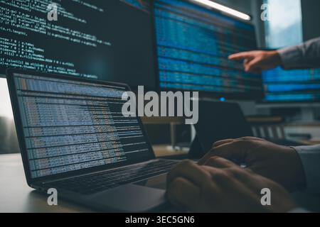 Developer programming code at a multi monitor workstation with laptop and screens displaying scripts, showing software development workflow, coding pr Stock Photo