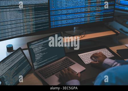 IT programmer working at a multi screen workstation with laptop and monitors displaying source code, showing software development workflow, coding pro Stock Photo