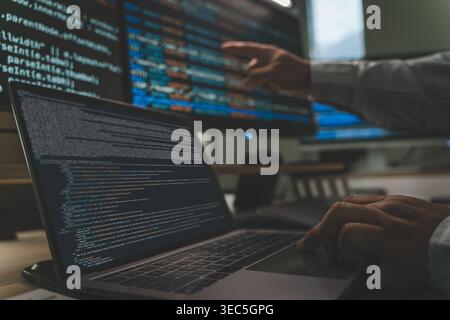 Developer programming code at a multi monitor workstation with laptop and screens displaying scripts, showing software development workflow, coding pr Stock Photo