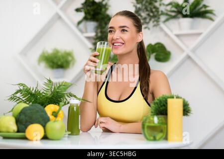 Woman Enjoying a Green Smoothie in a Healthy Kitchen Surrounded by Fresh Fruits and Vegetables Stock Photo