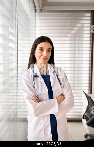 Smiling female doctor standing with arms crossed in clinic office Stock Photo