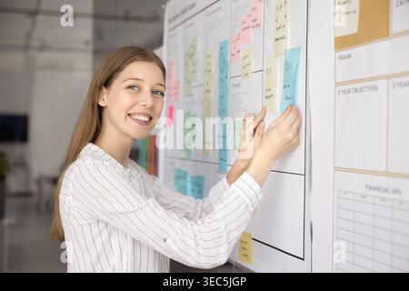 Female project manager placing or adjusting sticky notes Stock Photo