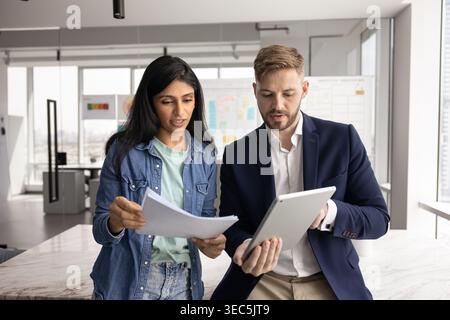Two teammates reviewing documents and data on tablet Stock Photo