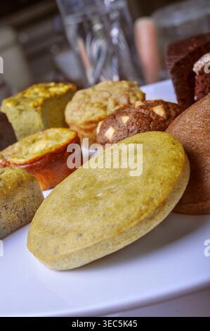 A close-up, high-angle shot of various mini muffins including matcha, chocolate chip, and whole grain varieties arranged on a clean white serving plat Stock Photo