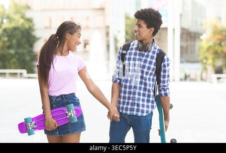 Two Young Friends Enjoy a Sunny Day Holding Hands While Skateboarding in the City Stock Photo