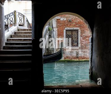 Venice, Italy, traditional gondola passing beneath a historic bridge on a narrow Venetian canal, a classic scene of the famous lagoon city. Stock Photo