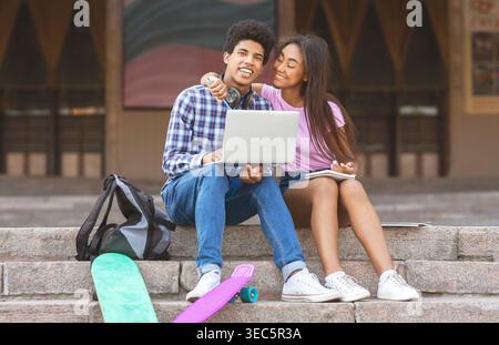 Two Students Enjoying Time Together on Steps With Laptop and Skateboards in a Sunny Setting Stock Photo