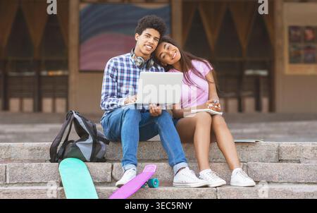 Young Couple Studying Together on Steps With Laptops and Skateboards at School Stock Photo