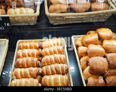 Customers browse through various freshly baked bread products in baskets at a store while shopping for their meals. Stock Photo