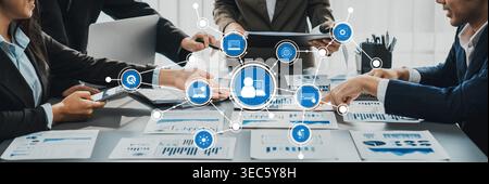 A professional team collaborates around a meeting table filled with charts and digital symbols, emphasizing teamwork and strategic planning for Stock Photo