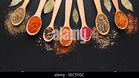 Various spices in wooden spoons on black background Stock Photo