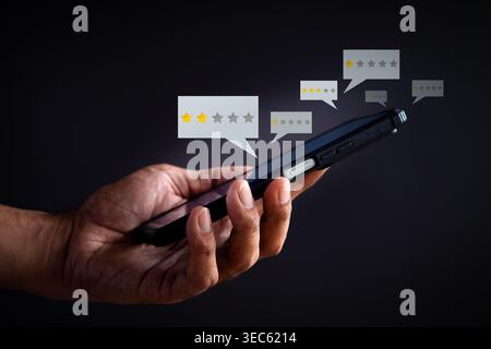 A hand holds a smartphone displaying low star rating bubbles on a dark background. Negative customer feedback, poor reviews concept. Stock Photo