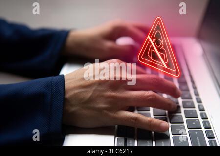 Close-up of hands typing on a laptop keyboard with a glowing red holographic warning triangle containing an anti-hacker symbol. Cybersecurity, hacking Stock Photo