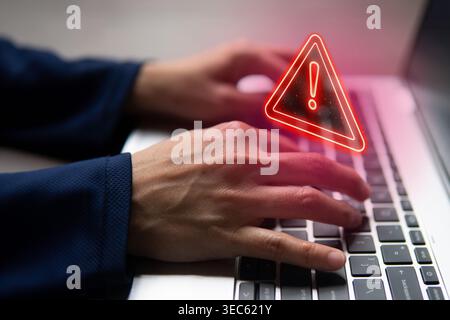 Hands typing on a laptop keyboard with a glowing red holographic warning triangle and exclamation mark. Cyber threat or security alert concept. Stock Photo