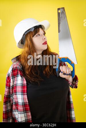 Woman wearing hard hat holding hand saw looking up Stock Photo