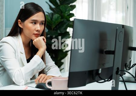Working young asian businesswoman focusing on pc searching new project base on marketing database online wearing white suit at modern home office Stock Photo