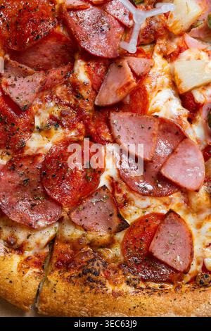 Close up of a freshly baked pizza with delicious toppings, cheese, pepperoni, ham, pineapple and other ingredients. Stock Photo