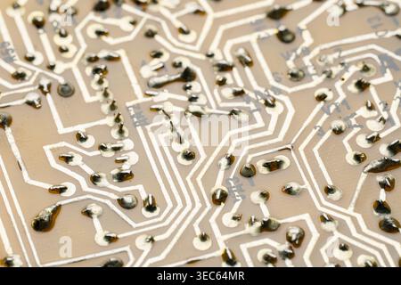 Macro photography of solder joints and copper tracks on a yellow printed circuit board. Technical background of electronic pathways and manual solderi Stock Photo