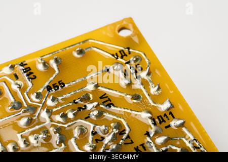 Macro photography of solder joints and copper tracks on a yellow printed circuit board. Technical background of electronic pathways and manual solderi Stock Photo