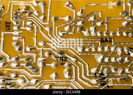 Macro photography of solder joints and copper tracks on a yellow printed circuit board. Technical background of electronic pathways and manual solderi Stock Photo